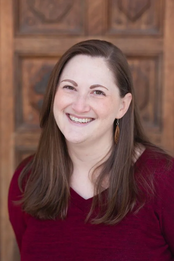 Picture of Rachel smiling, standing in front of a brown, wooden door.